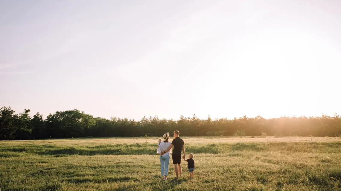 Familie mit Kind geht bei Sonnenuntergang über eine Wiese