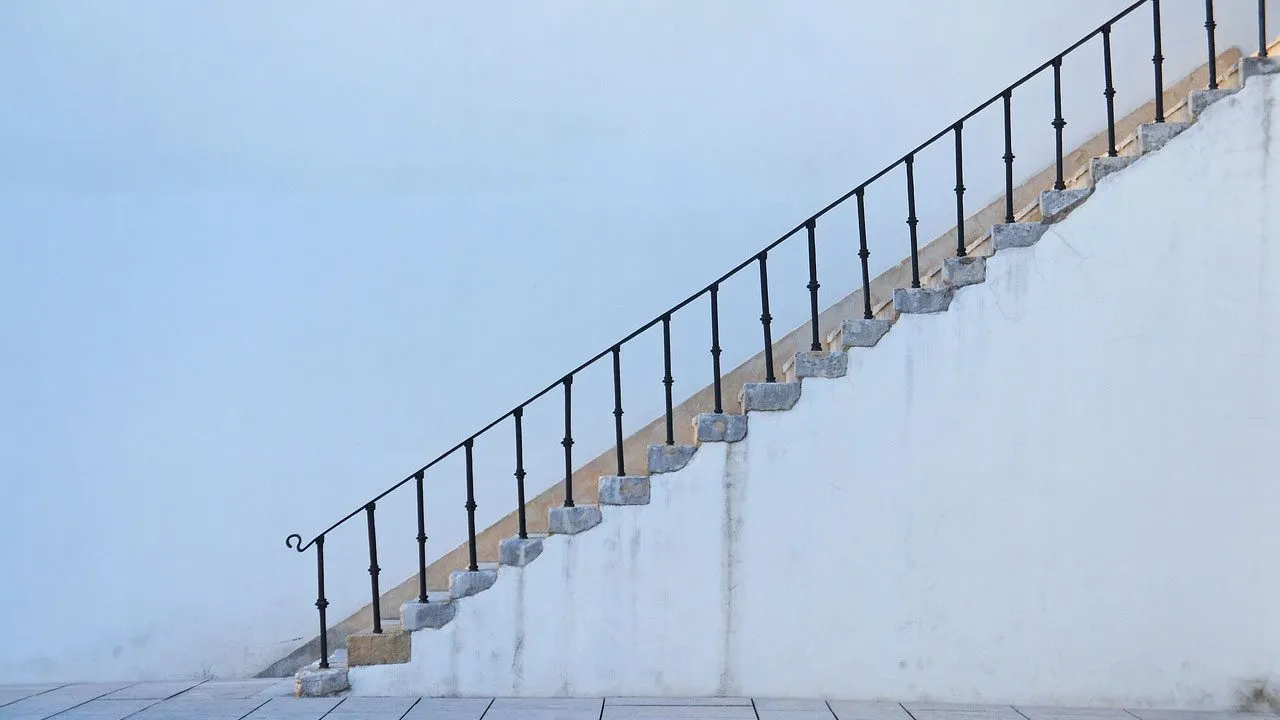 Steinerne Treppe mit schmiedeeisernem Geländer an einer weißen Wand