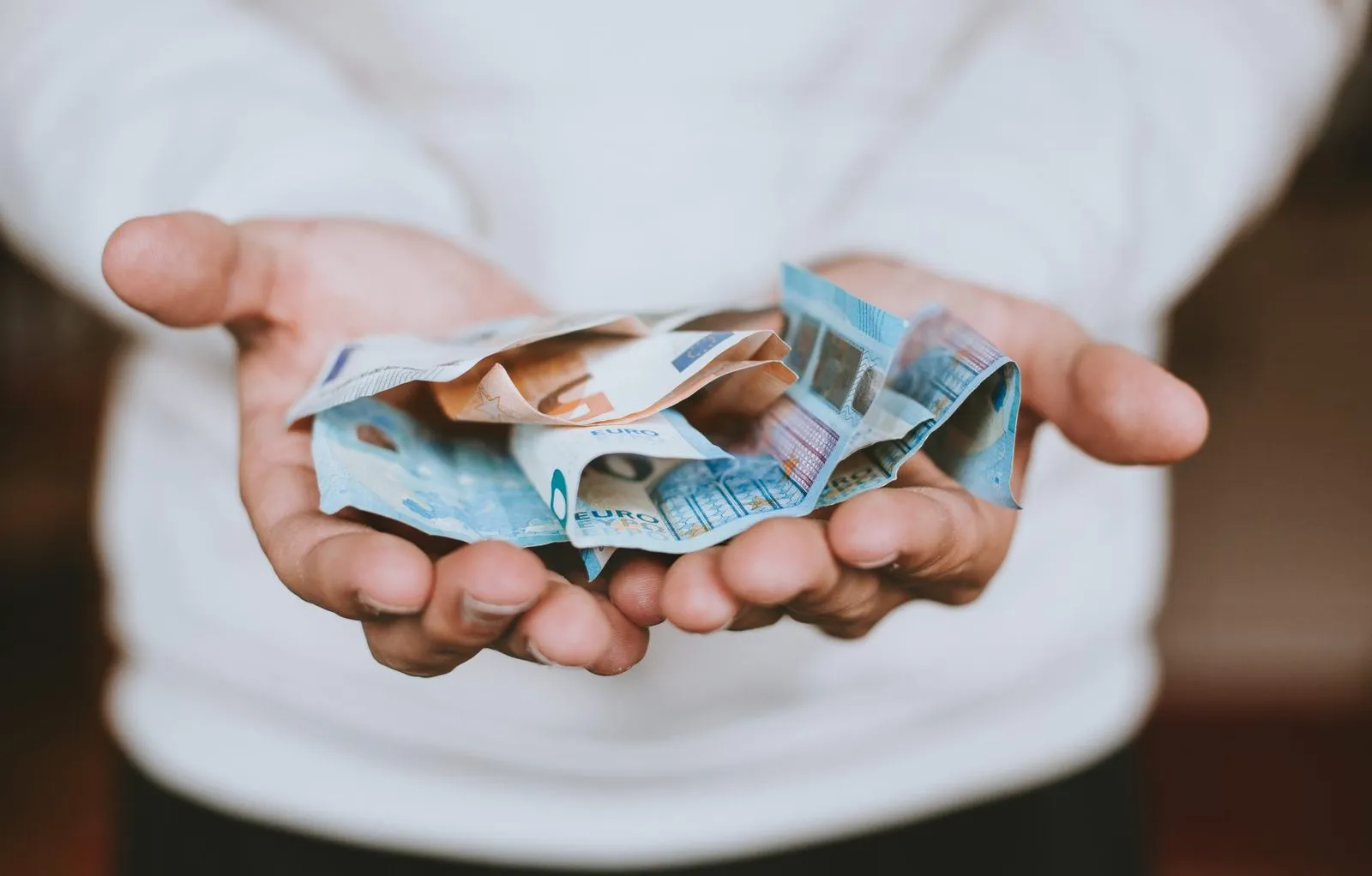 Zwei geöffnete Hände halten zerknitterte Euro-Geldscheine