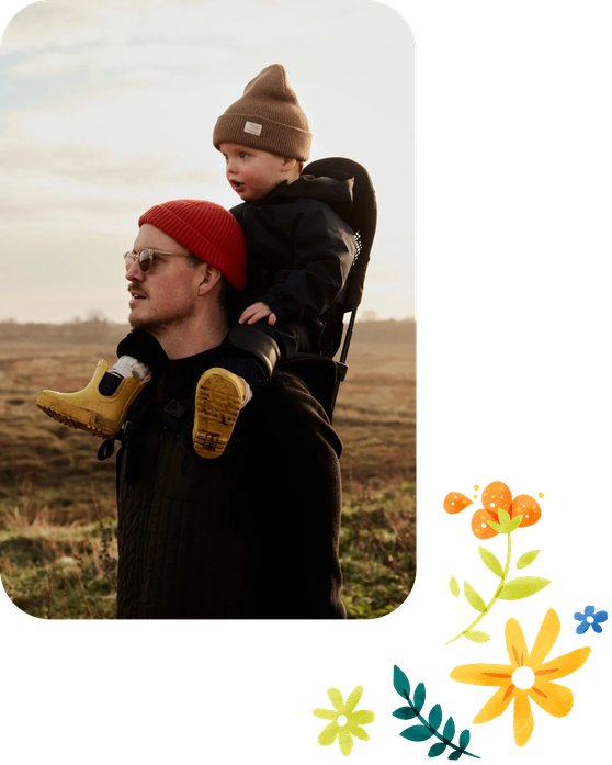 Ein Vater trägt seinen Sohn auf den Schultern durch die Natur.